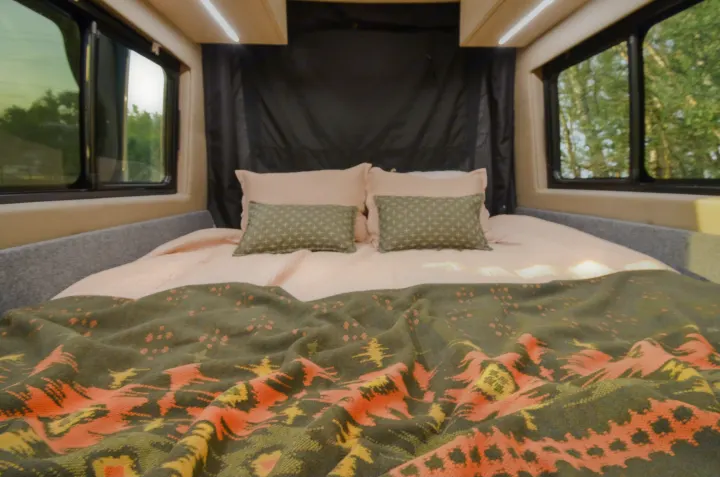 Comfortable RV rental bedroom featuring a full bed with cozy pink sheets, patterned pillows, and scenic window views.. Cahaba Cahaba Class B 2021