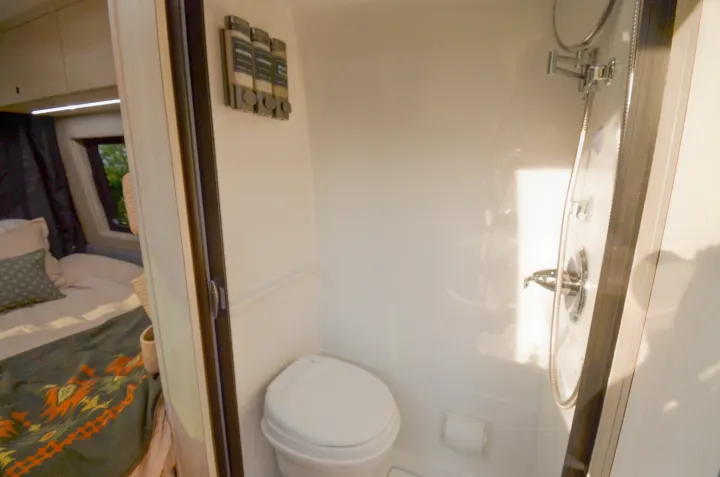 Inside an RV rental: a compact bathroom with toilet & shower, offering a glimpse into the connected cozy bedroom.. Cahaba Cahaba Class B 2021
