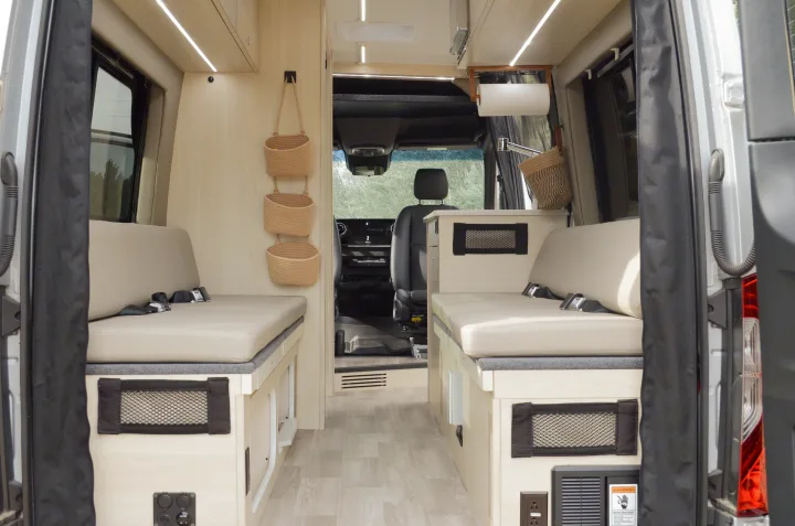 View of a modern rv rental interior: light wood, cushioned bench seats with seatbelts, and storage solutions.. Cahaba Cahaba Class B 2021