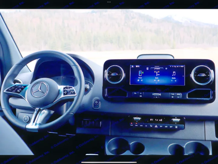 Dashboard of a Mercedes-Benz rv rental, featuring a modern steering wheel, infotainment display, and a scenic view of distant mountains.. Mercedes-Benz Sprinter 2025