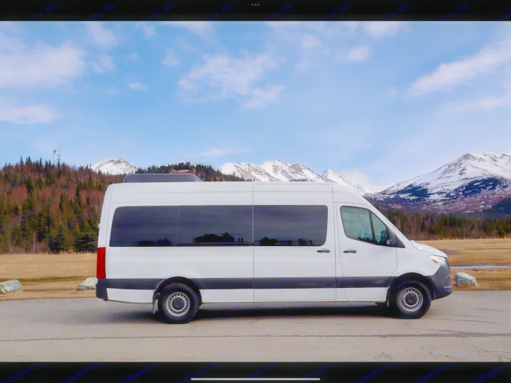 A white camper van, perfect for RV rental, is parked on a road against a backdrop of snow-capped mountains and blue sky.. Mercedes-Benz Sprinter 2025