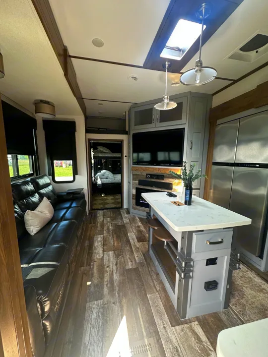 This modern RV rental living space has a comfy black sofa, kitchen island, TV area, and bunk beds beyond.. Keystone RV Fuzion Toy Hauler 2021