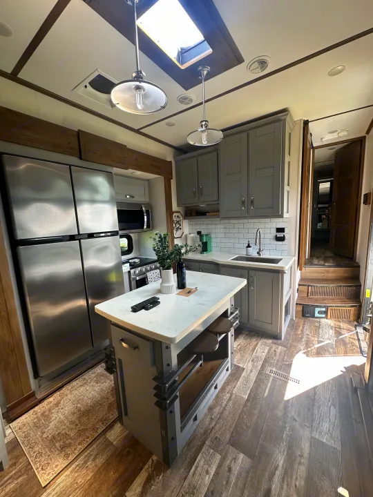 Bright, modern **RV rental** kitchen featuring a large fridge, island seating, gray cabinets, and a skylight for natural light.. Keystone RV Fuzion Toy Hauler 2021