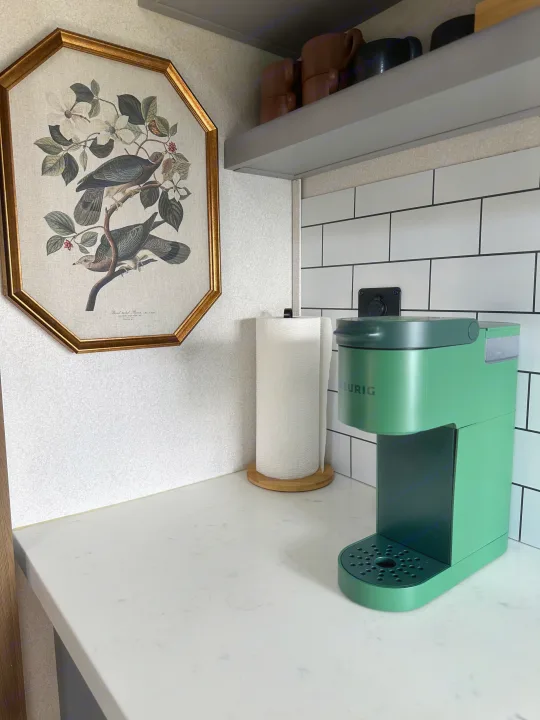 Compact kitchen in an RV rental, featuring a green Keurig, paper towels, framed bird art, and subway tile.. Keystone RV Fuzion Toy Hauler 2021