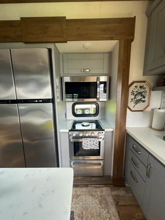 Compact RV rental kitchen features stainless appliances, gray cabinets, white counters, and a wooden trim design.. Keystone RV Fuzion Toy Hauler 2021