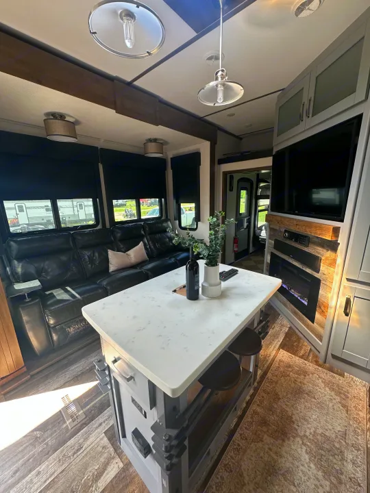 Inside this modern RV rental: a spacious living area with a kitchen island, comfy leather sofa, and entertainment center with fireplace.. Keystone RV Fuzion Toy Hauler 2021
