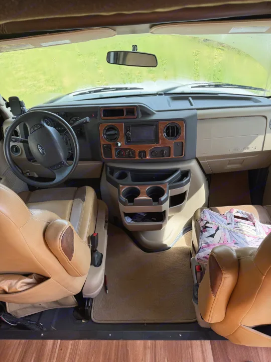 RV rental interior: The Ford E-Series cockpit with tan seats, dashboard, and steering wheel for drivers and passengers.. Jayco Greyhawk 2015