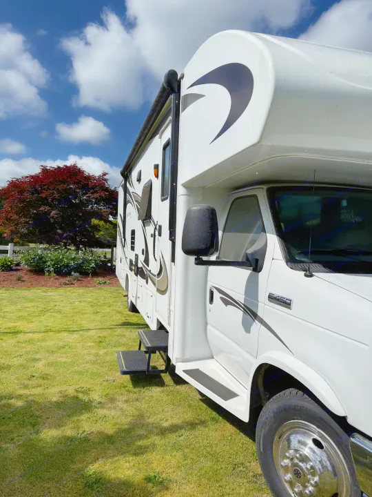 White Class C RV rental with graphic details parked on green grass under a blue sky, ideal for your next trip.. Jayco Greyhawk 2015