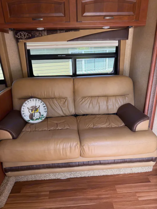 Comfortable tan leather sofa in an RV rental living area, featuring an owl thermometer, window, and wood cabinetry.. Jayco Greyhawk 2015