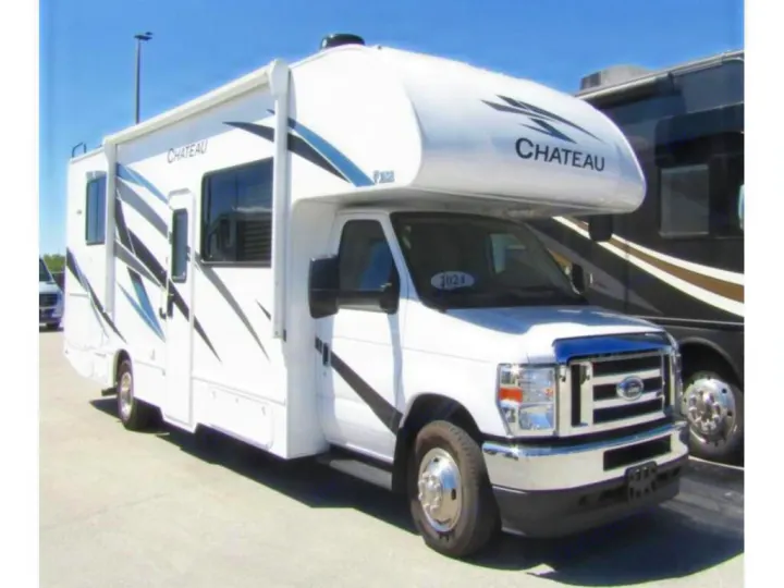 A clean white Chateau Class C RV with sleek black and blue decals, perfect for your next rv rental adventure, parked outdoors.. Thor Chateau 2024