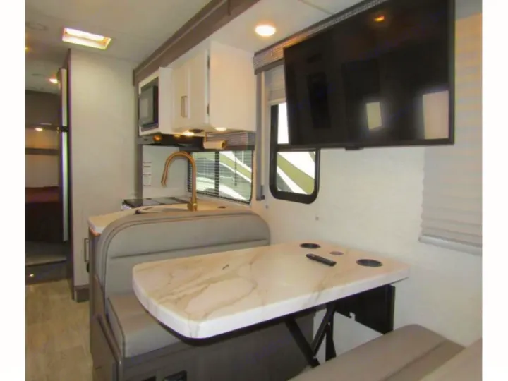 Modern RV rental interior: dinette with marble-look table, wall-mounted TV, and a compact kitchen area.. Thor Chateau 2024