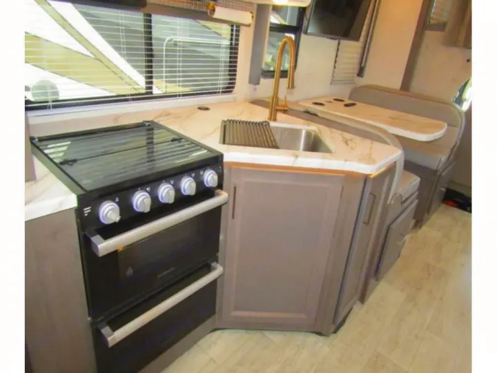 Modern RV rental kitchen features a black stove, gold faucet, white countertops, and an adjacent booth dining area.. Thor Chateau 2024