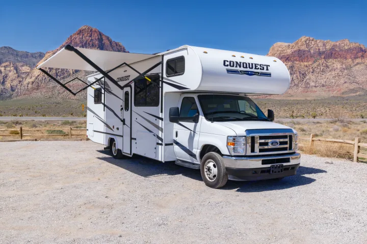 White Conquest RV rental with awning extended, parked in a scenic desert landscape with mountains under a clear sky.. Gulf Stream Conquest 2024