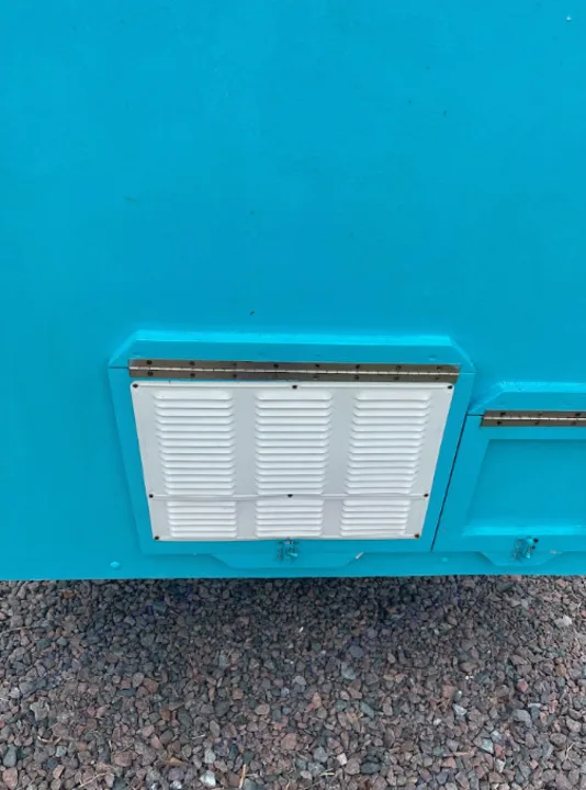 Bright blue RV exterior with a white louvered access panel for systems like refrigeration, common on an RV rental.. YNGQ Box 2017