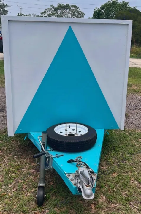 Custom blue trailer for RV rental advertising, featuring a striking white and blue triangle sign, with a spare tire.. YNGQ Box 2017