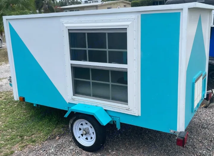 Teal & white RV rental trailer with a diagonal color design and a prominent side window.. YNGQ Box 2017