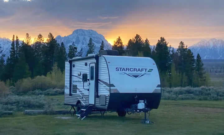 An RV travel trailer rental at a scenic mountain campsite, bathed in golden sunrise light. Ideal for outdoor adventures.. Starcraft Autumn Ridge 2023