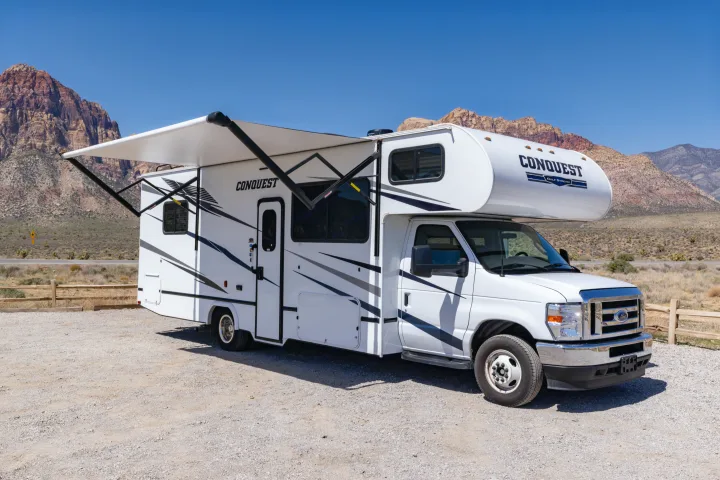 Conquest Gulf Stream RV rental with awning extended, parked on gravel in a scenic desert mountain area.. Gulf Stream Conquest 2024