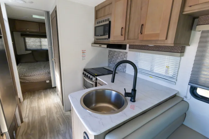 Inside an RV rental: a modern kitchen with a sink and stove, dining bench, and a view into the cozy bedroom.. Gulf Stream Conquest 2024