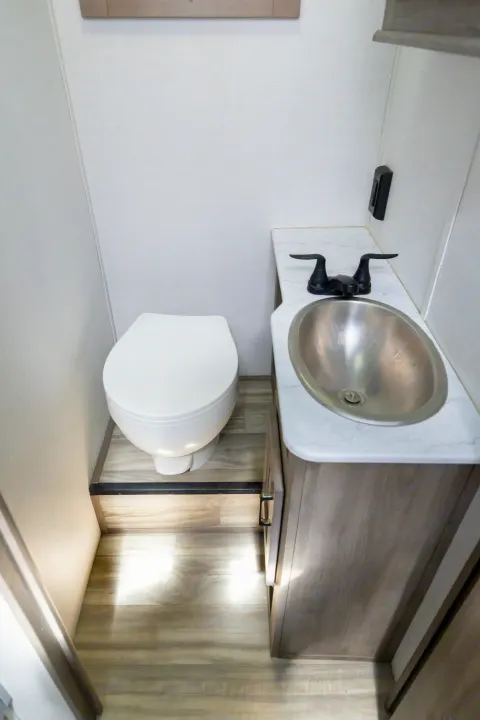 RV rental bathroom showing compact toilet, sink with black faucet, and vanity on wood-look floor.. Gulf Stream Conquest 2024