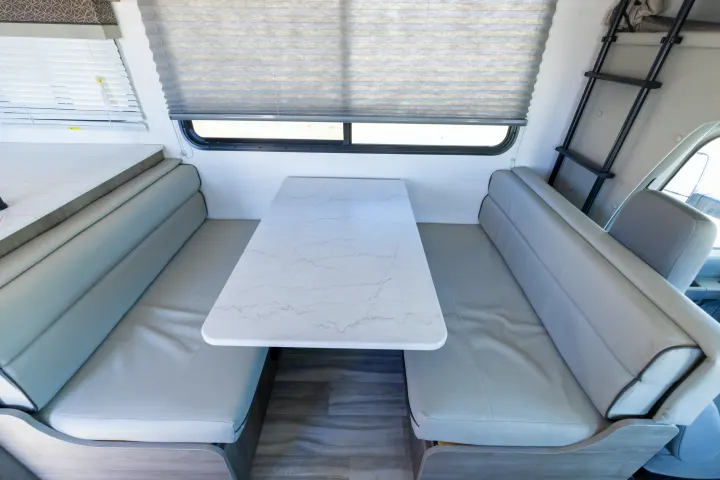 RV rental dinette with marble-look table and gray cushioned benches, offering comfortable dining and seating.. Gulf Stream Conquest 2024
