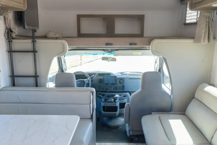 Interior of an rv rental, showcasing the driver's cockpit, dinette, and overhead sleeping bunk.. Gulf Stream Conquest 2024