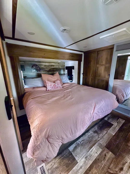 Spacious RV rental bedroom with a large bed, wood-paneled headboard, and mirrored closet. Perfect for travel.. Keystone RV Fuzion Toy Hauler 2021