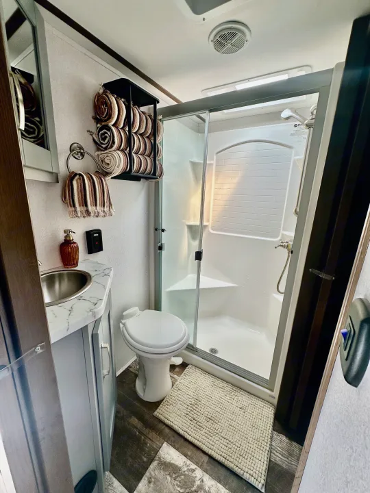 RV rental bathroom: A clean, bright space with a sliding glass shower, toilet, sink vanity, and striped towels.. Keystone RV Fuzion Toy Hauler 2021