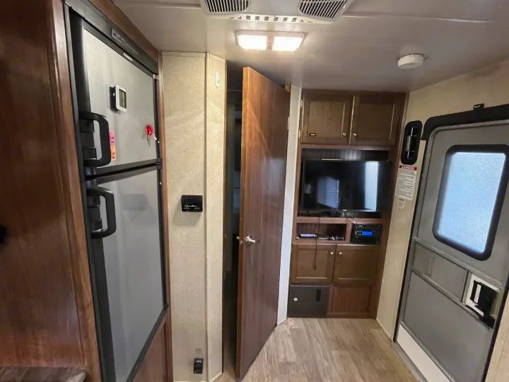 Bright RV rental interior, showcasing the refrigerator, entertainment center, and a glimpse into the sleeping quarters.. Heartland Prowler 2019