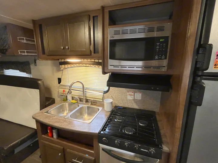 RV rental kitchen featuring a double sink, gas stove, microwave, and cabinetry. A well-equipped space for meals on the go.. Heartland Prowler 2019