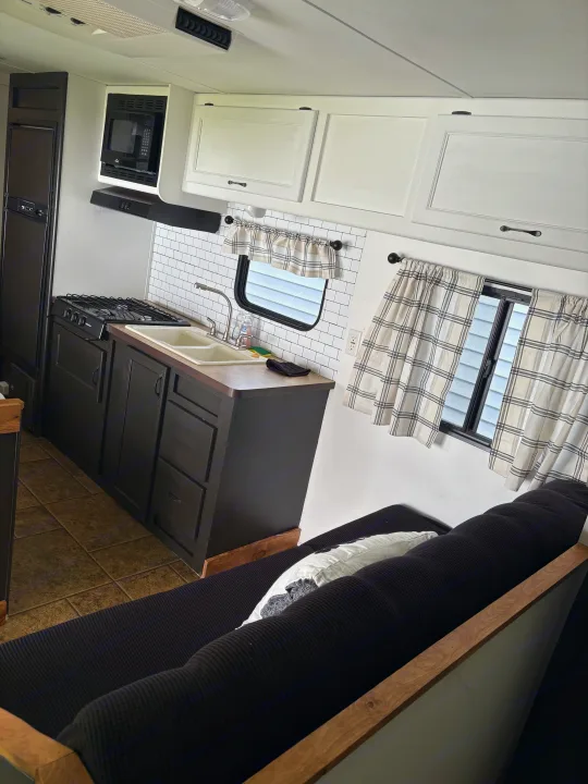 Modern RV rental kitchen featuring black cabinets, a stove, sink, and white subway tile backsplash, with a comfy black sofa nearby.. Forest River Cherokee Grey Wolf 2012