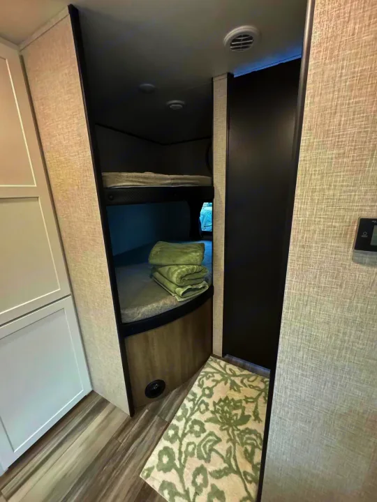 Compact RV rental interior with bunk beds, neatly folded towels, and a cozy rug. Ideal for family travel.. Jayco JAY Flight SLX 261BHS 2025