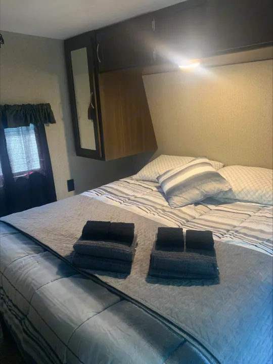 Cozy RV rental bedroom featuring a comfortable bed, fresh towels, overhead cabinets, and a window.. Keystone RV Springdale 2019