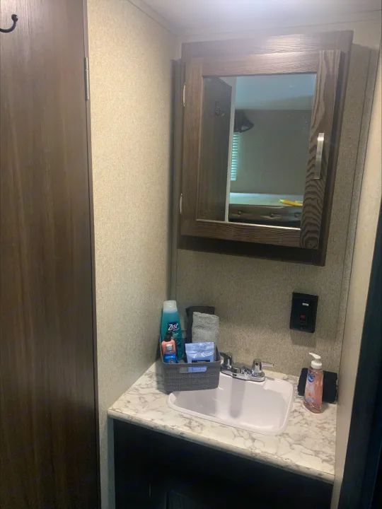 RV rental bathroom: compact vanity with sink, faucet, medicine cabinet mirror, and toiletries. Light walls, wood cabinetry.. Keystone RV Springdale 2019