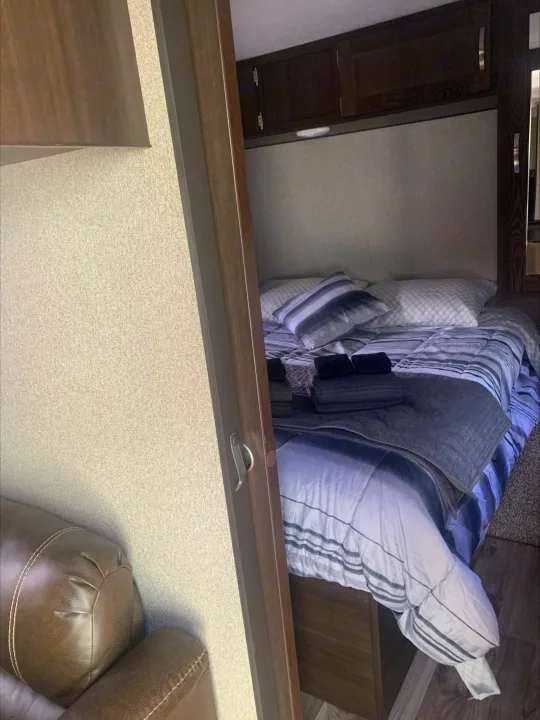 RV rental: A modern bedroom with striped bedding, pillows, and dark wood overhead cabinets.. Keystone RV Springdale 2019