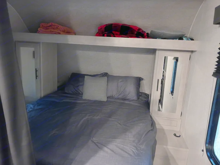 This RV rental bedroom features a comfy bed with dark bedding, overhead shelf, and mirrored storage.. Crossroads Zinger Lite 2025