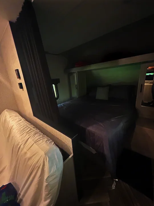 Inside a cozy RV rental bedroom with a grey bed, overhead storage, and a white couch, ready for your next trip.. Crossroads Zinger Lite 2025