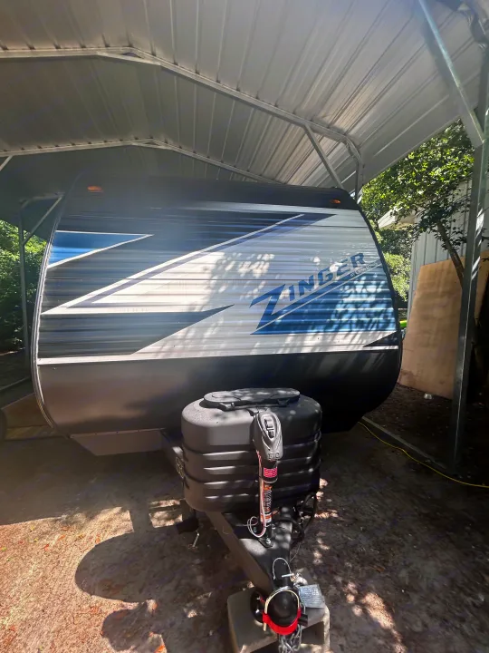 A Zinger travel trailer (RV) rental by Crossroads, parked under a metal carport outdoors.. Crossroads Zinger Lite 2025
