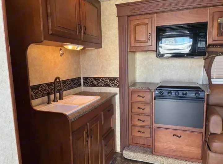 Modern RV rental kitchen featuring rich wood cabinets, double sink, microwave, and stove for convenient cooking on the road.. Jayco Greyhawk 2011