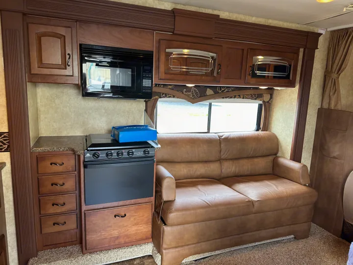 This RV rental's interior features a brown leather couch, a microwave, stove, and wood cabinetry.. Jayco Greyhawk 2011