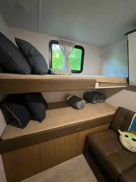 Inside an RV rental: a stacked bunk bed area with dark pillows, a bright window, and a lower lounge seat. Ideal for families.. Forest River 273QBXL 2025