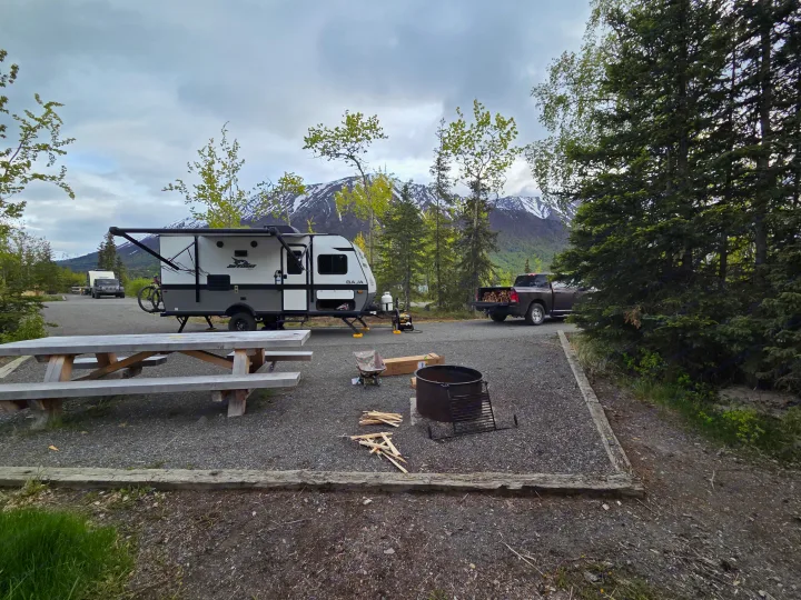Scenic RV rental campsite featuring a white travel trailer, picnic table, fire pit, and snow-capped mountains.. Jayco Jay Flight SLX Baja Edition 2022