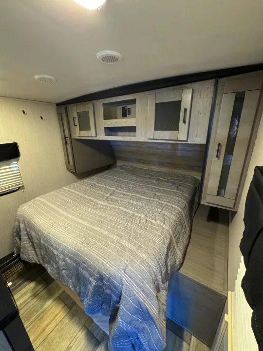 Cozy RV rental bedroom with a grey striped bed, overhead storage cabinets, and ceiling vents.. Heartland RVs North Trail 2021