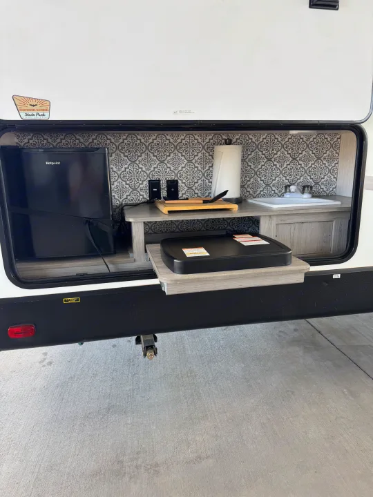 This RV rental's outdoor kitchen features a Hotpoint mini-fridge, sink, and griddle, ideal for outdoor cooking.. Heartland RVs North Trail 2021