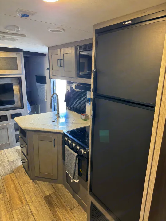 Inside a clean RV rental, featuring a modern kitchen with a large fridge, island, stove, and TV area.. Heartland RVs North Trail 2021