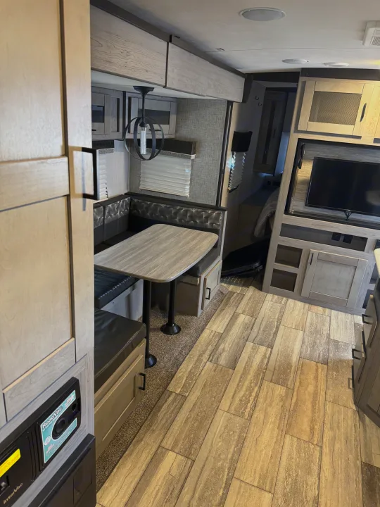 RV rental interior: large dinette booth, modern TV setup, light wood cabinets, and stylish plank flooring.. Heartland RVs North Trail 2021