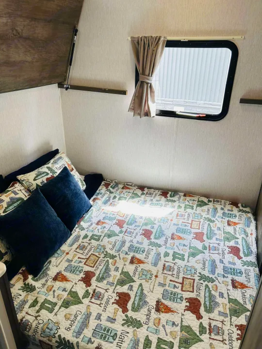 RV rental sleeping area featuring a camping-themed bed, cozy blue pillows, and window, ready for adventure.. Forest River Salem Cruise Lite 2022