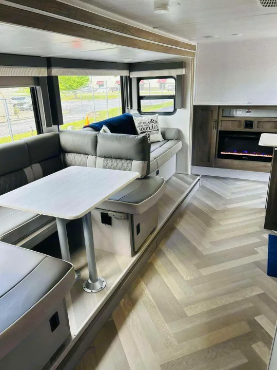 Inside a cozy RV rental: light wood herringbone floors, L-shaped dinette, lounge area, and fireplace create a welcoming space.. Forest River Salem Cruise Lite 2022
