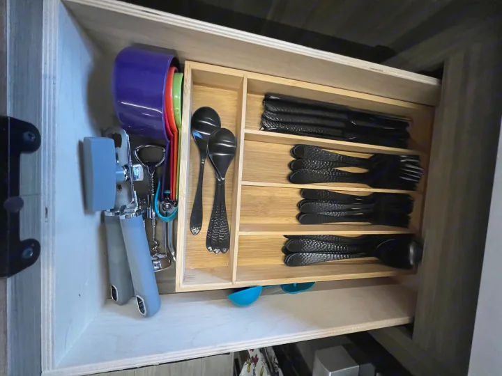 Compact and organized kitchen drawer in an RV rental, with silverware, measuring cups, and essential utensils.. Forest River 273QBXL 2025