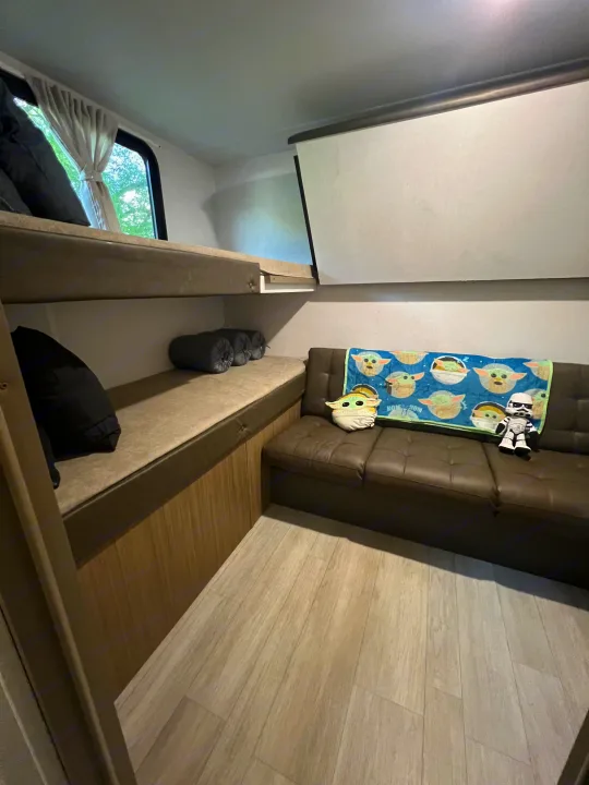 Bright RV rental interior: upper bunk, lower sleeping area, brown sofa with Grogu & Stormtrooper, wood floor.. Forest River 273QBXL 2025